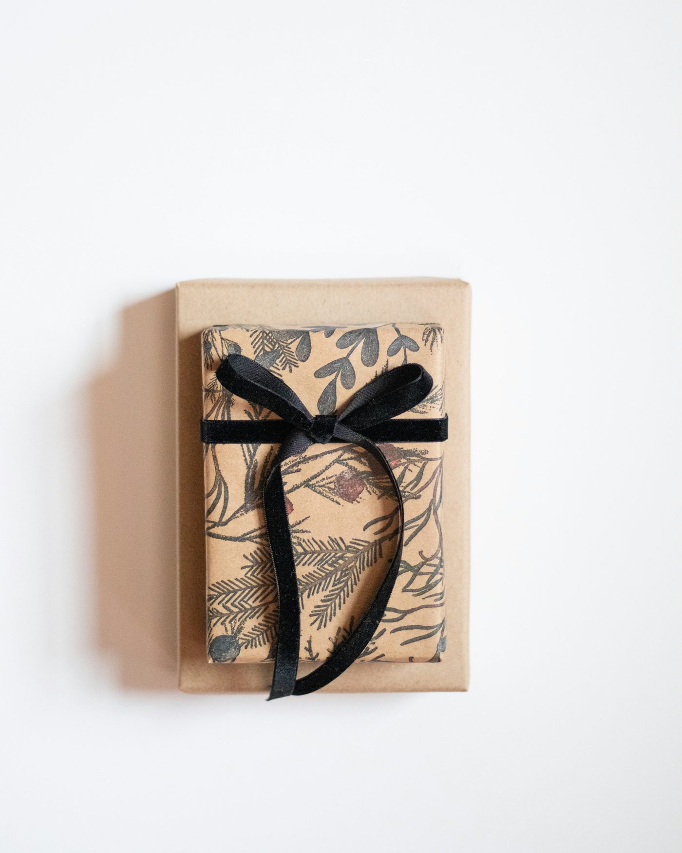 A small gift wrapped in botanical paper and tied with black velvet ribbon on a pale ground