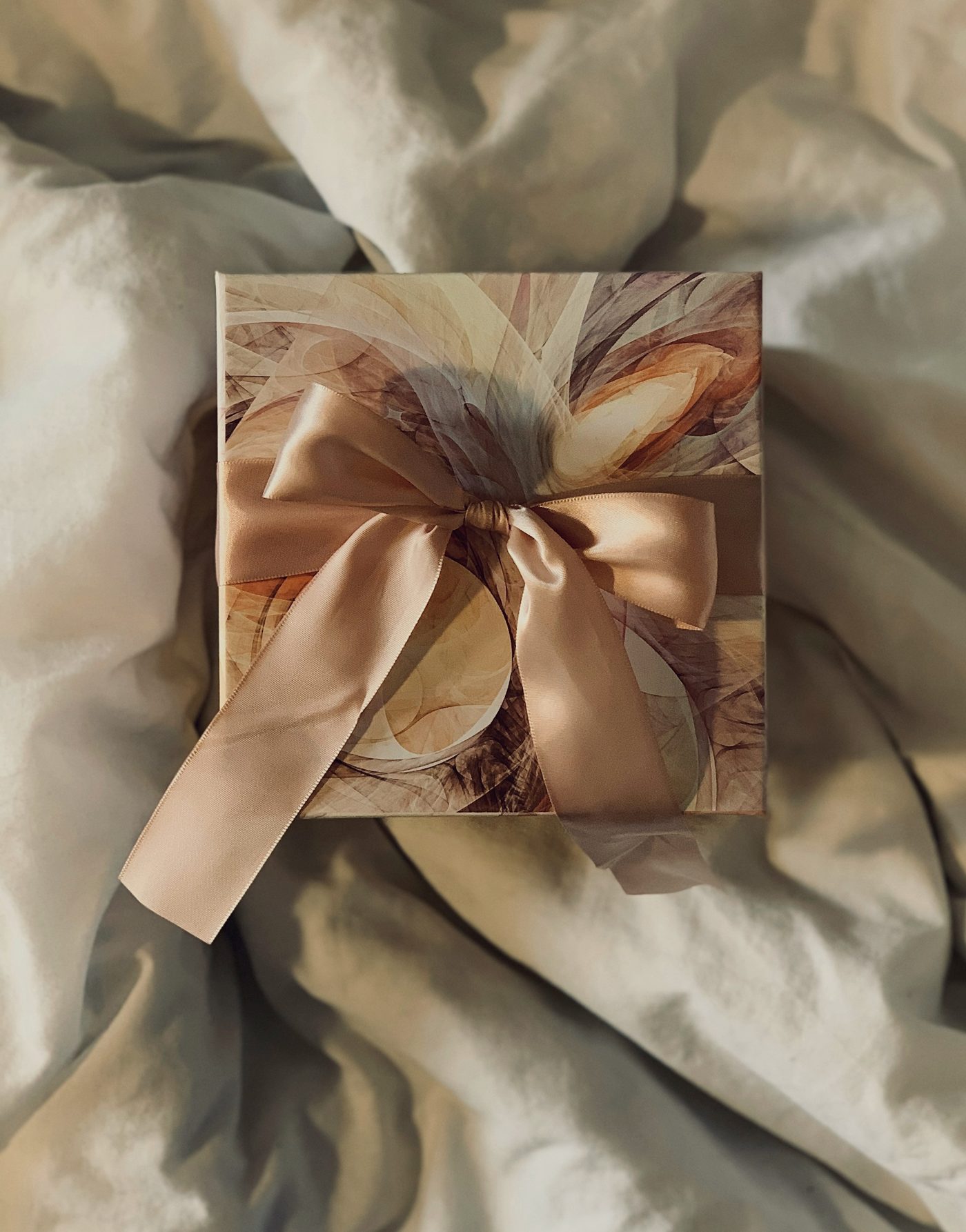A wrapped gift tied with a wide champagne silk ribbon, resting on soft white linen